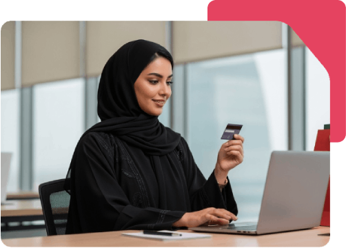 Woman in black hijab shops online using laptop and credit card.